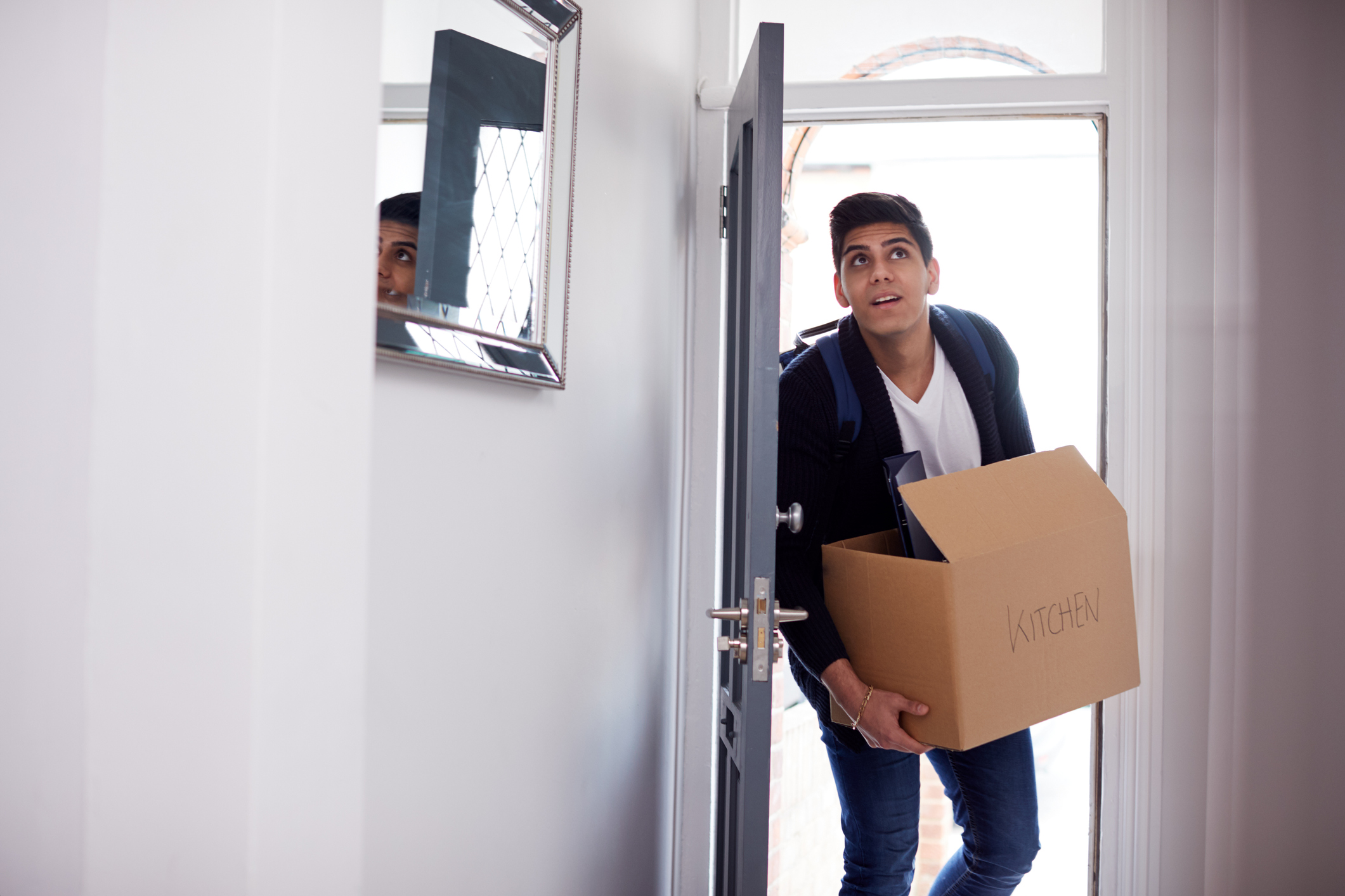 A man walking in the front door with a box in his hand, indicating he is in the middle of moving.